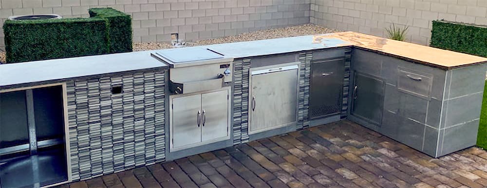 Outdoor kitchen with stone masonry around appliances and a brick patio